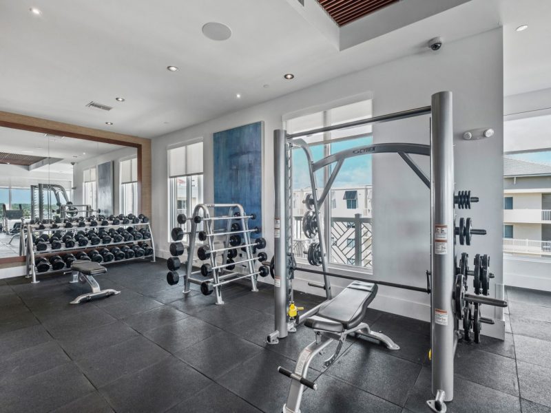 This image shows an expansive view of the 24-hour State-of-the-art fitness gym featuring different equipment that is essential for community amenities. The Athletic Club is offering a spacious area that was accessible to everyone and bringing up the different weight of dumbells that were good for strength and chest workout.