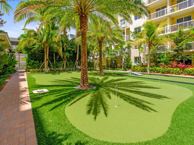 This image shows the TGM Harbor Beach Apartments Putting Green with a grassy golf fairway and lush trees that were a place for leisure and recreational activity.